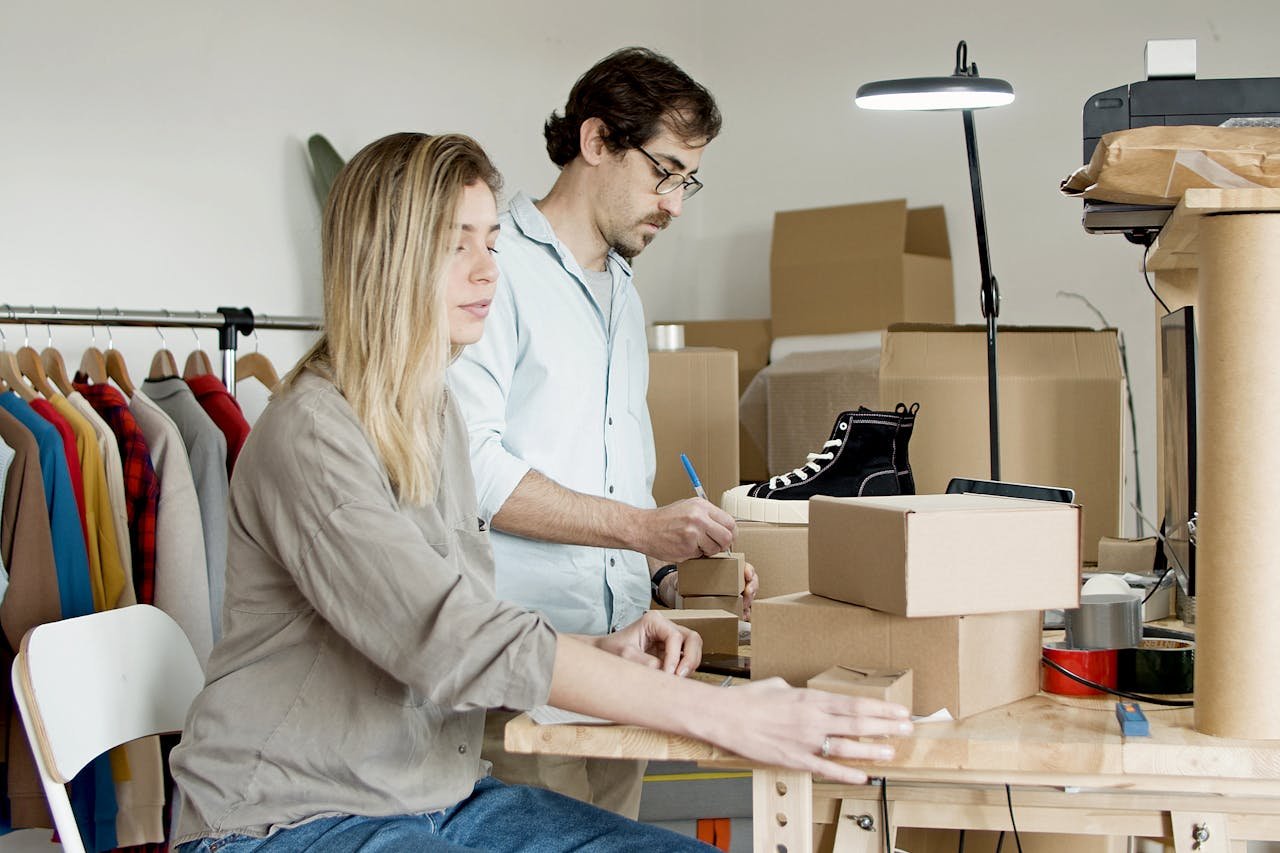 Business partners organizing inventory in an online store setup with clothes and boxes.